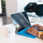 Hands typing on a blue keyboard with a branded cup on a table.
