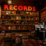 Warm interior view of a record store with vintage vinyls, retro decor, and a neon 'Records' sign.